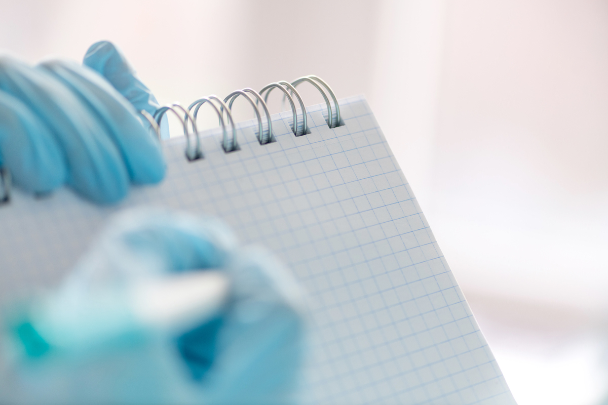 Female hand in a medical glove holds a tablet for writing and a pen