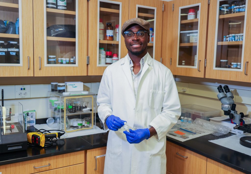 student in a lab coat in front of lab equipment