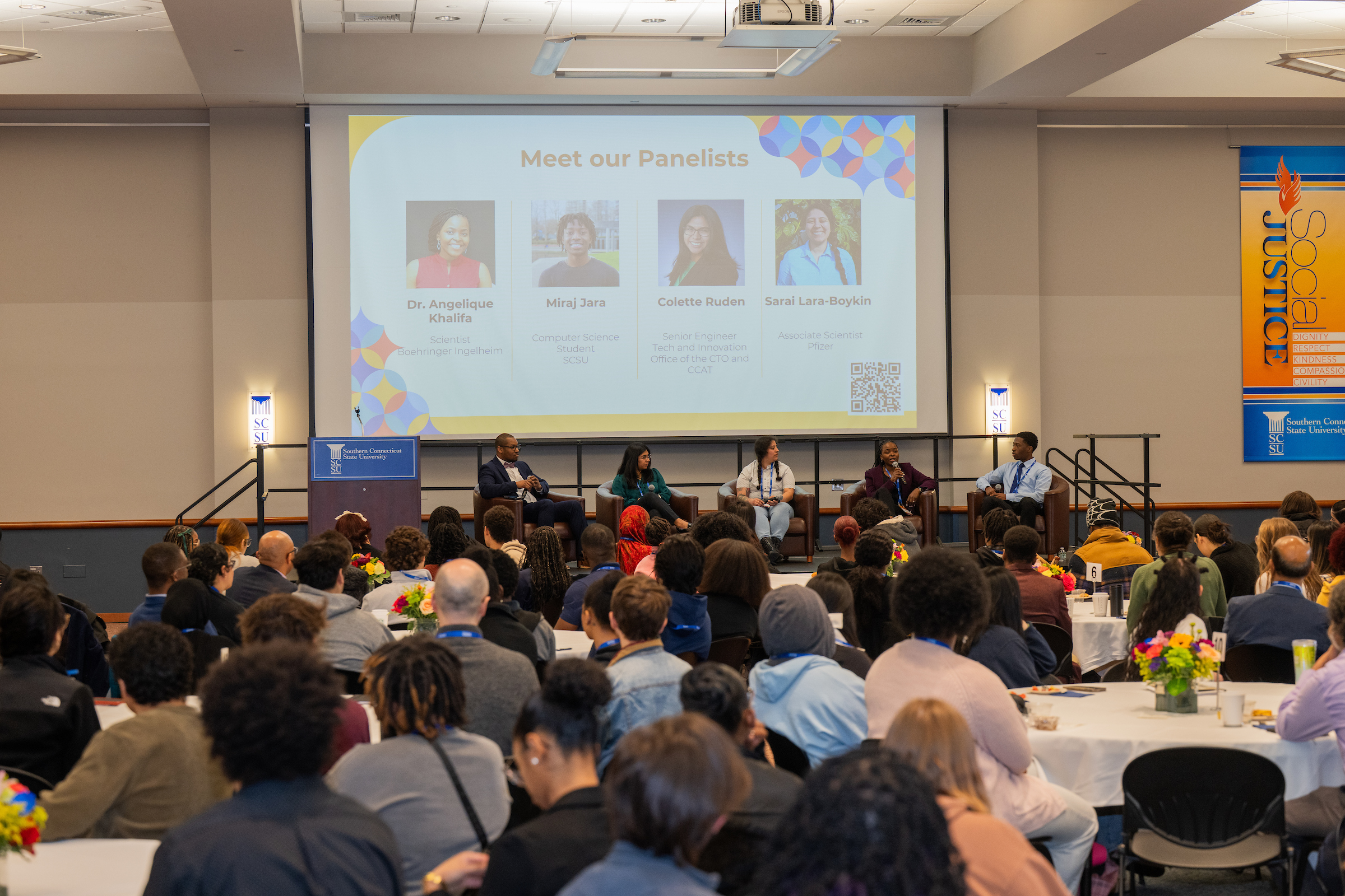 conference attendees sitting and listening to panelists on a stage